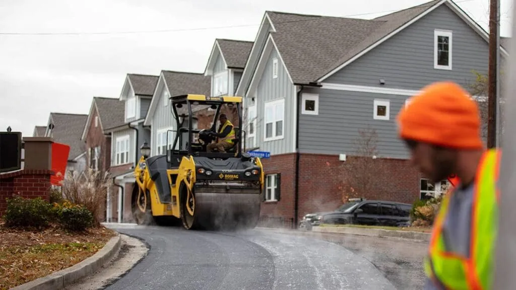 asphalt roller driving down a street with houses